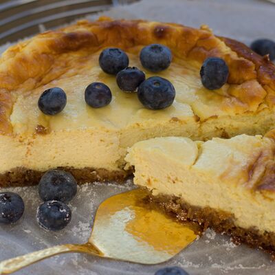 Bild vergrößern: Ksekuchen mit ein paar Blaubeeren garniert, ein goldener Tortenheber liegt auf dem Teller