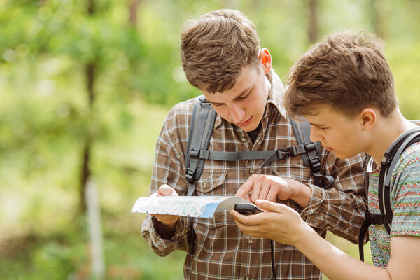 Zwei Jungs schauen auf eine Karte und haben ein Geocaching-Gerät in der Hand