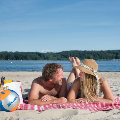 Bild vergrößern: Ein Mann und eine Frau liegen auf einer Decke am Strand.