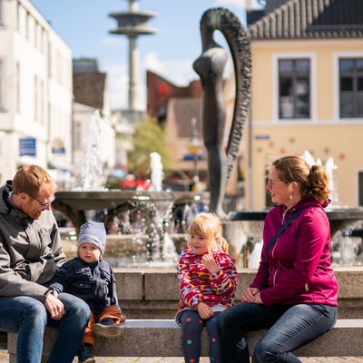 Bild vergrößern: Ein Mann und eine Frau sitzen mit ihren Kindern am Brunnen auf dem Marktplatz von Bad Segeberg.