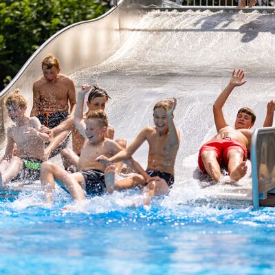 Bild vergrößern: Kinder rutschen eine Wasserrutsche in ein Schwimmbecken hinunter