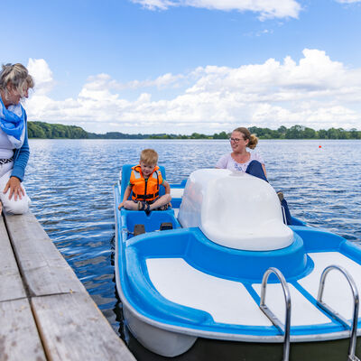 Bild vergrößern: Eine Frau mit Kind sitzt im einem Tretboot auf dem See. Eine Frau auf dem Steg spricht zu ihnen.