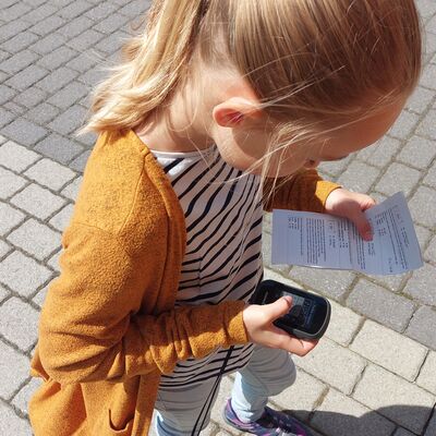 Bild vergrößern: Ein Mädchen mit gelber Strickjacke hält ein Geocaching-Gerät in der Hand