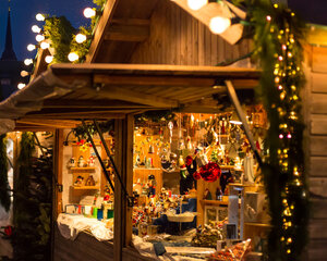 Bild vergrößern: Weihnachtlicher Marktstand mit Holzspielzeug, Christbaumschmuck und Lichterketten auf dem Bad Segeberger Weihnachtsmarkt bei Dämmerung.