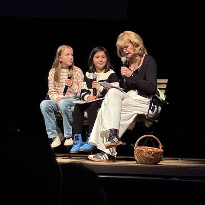 Bild vergrößern: Drei Personen sitzen auf einer Bühne im Kleinen Theater Wahlstedt, zwei Kinder mit Mikrofonen und eine Erwachsene mit Mikrofon und Korb auf dem Boden.