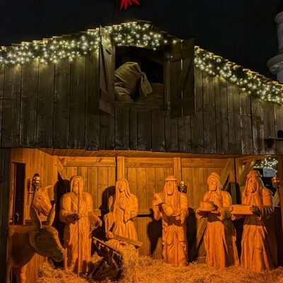 Bild vergr&ouml;&szlig;ern: Krippenszene mit h&ouml;lzernen Figuren von Maria, Josef, den Heiligen Drei K&ouml;nigen und einem Esel, beleuchtet und mit Stroh bedeckt, auf dem Weihnachtsmarkt Bad Segeberger Winterzauber.